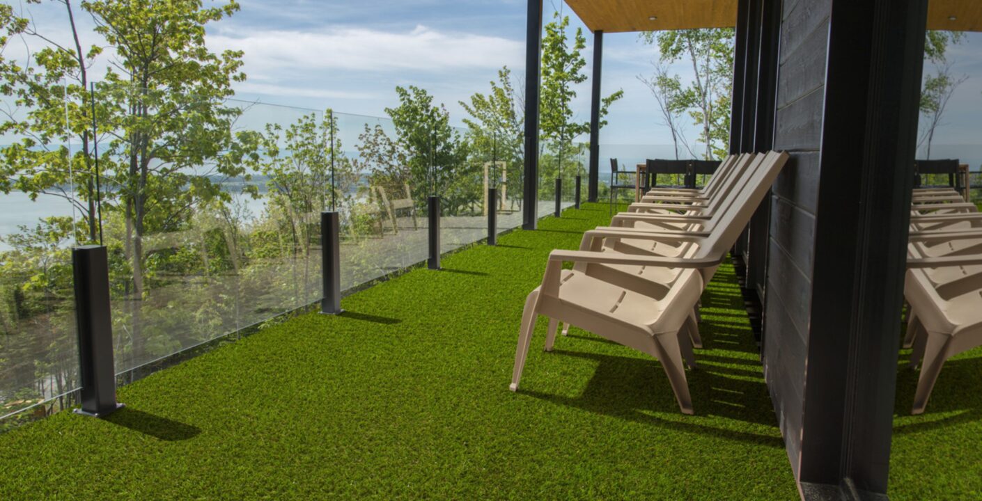Terrazza moderna con pavimentazione in prato sintetico misto erba Eurogreen, con vista panoramica e sedie da esterno beige.