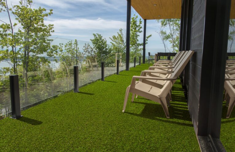 Terrazza moderna con pavimentazione in prato sintetico misto erba Eurogreen, con vista panoramica e sedie da esterno beige.
